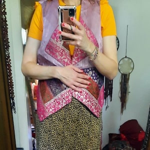 Könnte beinhalten: Ein Patchwork-Weste- und Rock-Ensemble. Die Weste ist helllila mit rosa floralen Akzenten und einem V-Ausschnitt. Der Rock hat ein Leopardenmuster. Das Outfit wird über einem gelben Oberteil getragen.