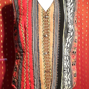 Könnte beinhalten: Eine gesteppte Weste mit V-Ausschnitt und Knopfverschluss. Die Weste hat ein Patchwork-Design mit vertikalen Streifen in Rot, Schwarz, Braun und Weiß. Die Weste wird auf einer Schaufensterpuppe präsentiert.