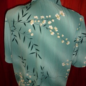K&ouml;nnte beinhalten: Ein kurz&auml;rmeliges, knopfverschlossenes Hemd in Tealblau mit einem wei&szlig;en Blumenmuster. Das Hemd hat einen Kragen und eine Knopfleiste vorne.