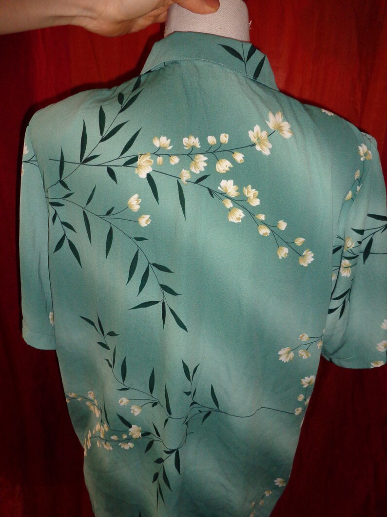 K&ouml;nnte beinhalten: Ein kurz&auml;rmeliges, knopfverschlossenes Hemd in Tealblau mit einem wei&szlig;en Blumenmuster. Das Hemd hat einen Kragen und eine Knopfleiste vorne.