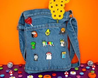 May include: A blue denim tote bag with a variety of colorful enamel pins attached to it. The pins feature various designs, including cats, avocados, and a frog. A bouquet of yellow sunflowers is peeking out of the top of the bag.