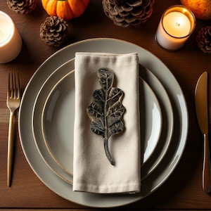 Hand-forged oak leaf in black finish on linen napkin, close-up.