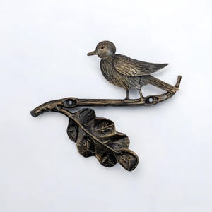 May include: A cast iron bird on a branch with an oak leaf. The bird and branch are painted in a gold finish.