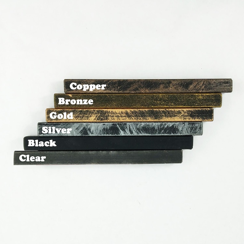 K&ouml;nnte beinhalten: Ein Satz aus sechs Holzleisten in verschiedenen Farben, darunter Kupfer, Bronze, Gold, Silber, Schwarz und Klar. Die Leisten sind &uuml;bereinander gestapelt, wobei die Kupferleiste oben und die klare Leiste unten liegt.