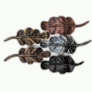 K&ouml;nnte beinhalten: F&uuml;nf Eichenblatt-Dekorationen aus Metall in Gold, Bronze, Silber, Schwarz und Kupfer. Jedes Blatt hat detaillierte Adern und einen Stiel. Diese dekorativen Bl&auml;tter sind ideal f&uuml;r Herbstdekorationen.