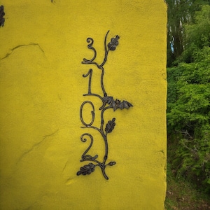 Puede incluir: Una pared amarilla con un diseño de vid en metal negro con hojas y los números 3102.