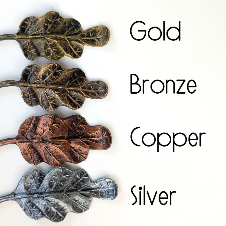 K&ouml;nnte beinhalten: Vier Metallblatt-Ornamente in Gold, Bronze, Kupfer und Silber. Die Bl&auml;tter haben detaillierte Adern und sind vertikal angeordnet. Die W&ouml;rter "Gold", "Bronze", "Copper" und "Silver" sind in schwarzer Schrift neben jedem Blatt geschrieben.