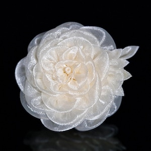 Könnte beinhalten: Eine weiße Stoffblume mit einem mehrschichtigen, gekräuselten Design. Die Blume ist aus durchsichtigem Stoff gefertigt und hat ein zartes, weibliches Aussehen.