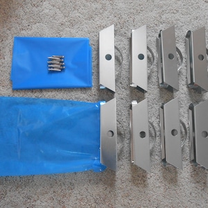 May include: Eight silver-colored metal rollers with a small hole in the center of each. The rollers are arranged in two rows of four. There are also two blue plastic bags and a small bag of silver screws.