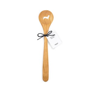 Puede incluir: Una cuchara de madera con un dise&ntilde;o de dachshund recortado. La cuchara est&aacute; hecha de madera natural y tiene una cuerda negra atada alrededor del mango con una etiqueta blanca que dice "Kuchen Helfer" y "Seesucht".