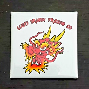 May include: A white square sticker with a red and yellow cartoon dragon head. The text "Lucky Dragon Trading Co." is written in red above the dragon.