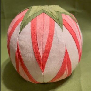 May include: A pink and green fabric ball with a star-shaped design. The ball is made of fabric strips sewn together to create a 3D effect.