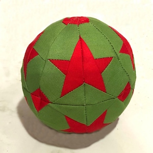 Puede incluir: Una bola de tela verde y roja con un patrón de estrellas. La bola está hecha de tela y está cosida.