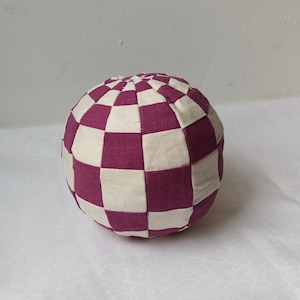 Puede incluir: Una esfera decorativa de tela con cuadros blancos y morados.