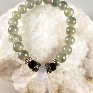 May include: Iridescent beaded bracelet with a central design. The bracelet features large, round, opalescent beads. Accented with black lava beads, silver-toned spacers, and a pearlescent stone. A unique piece of jewelry.