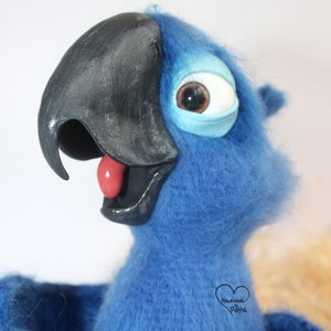 May include: Blue and black felt parrot plush toy with a large, round eye. The parrot has a red tongue sticking out and is looking to the right. The toy is handmade and has a tag that says "Handmade by Portik".