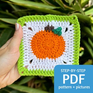 Op de afbeelding: Een gehaakt vierkant met een groene rand, een wit centrum en een oranje pompoen in het midden. Het vierkant wordt in een hand gehouden. De tekst "STEP-BY-STEP PDF pattern + pictures" staat onder het vierkant.
