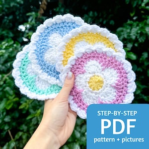 Könnte beinhalten: Vier gehäkelte Blumen-Untersetzer in Pastellfarben: hellblau, gelb, grün und rosa. Die Untersetzer haben eine weiße Mitte mit einer kleineren gelben Mitte. Das Bild enthält den Text "STEP-BY-STEP PDF pattern + pictures".