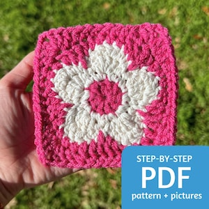 May include: A crochet square with a pink border and a white flower in the center. The flower has a pink center. The text "STEP-BY-STEP PDF pattern + pictures" is below the square.