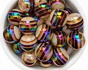 May include: A collection of spherical beads in a white bowl. Each bead features alternating horizontal stripes of cream-colored material and a dark, iridescent metallic finish that reflects rainbow colors under light. The beads are round and smooth.