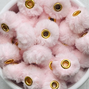 May include: A bowl filled with pink fluffy pom poms with gold eyelets. The pom poms are soft and plush.
