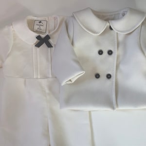 Può includere: Un completo bianco per neonato con una giacca a doppio petto e una camicia a maniche lunghe con un fiocco nero. La camicia ha un'etichetta che recita "bonbon in fête".