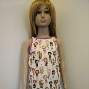 Könnte beinhalten: Ein weißes Tanktop mit einem sich wiederholenden Muster von Cartoon-Mädchen in verschiedenen Outfits. Das Oberteil hat eine lila Einfassung um den Halsausschnitt und die Armausschnitte. Die Schaufensterpuppe trägt auch eine blaue Jeans.
