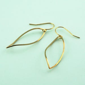 May include: A pair of gold-colored, leaf-shaped earrings. Each earring features a delicate, open design with a curved, elongated shape. The earrings hang from simple, curved ear wires, showcasing a minimalist aesthetic.