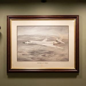 May include: A wall display featuring a military service cap, a framed print of a North American B-1 bomber, a shadow box with three medals, a framed Air Force emblem, a framed black and white photograph of a flight crew, and a brass nameplate.