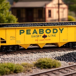 May include: A yellow model train coal car with the text "PEABODY SHORT LINE" in green. The car is filled with black coal and sits on a model railroad track. The words "the coal route" are also printed on the side.