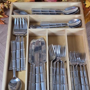 May include: A rectangular bamboo cutlery organizer tray containing a set of stainless steel flatware. The silverware features a distinct bamboo-style textured handle design, including forks, knives, and spoons arranged in separate compartments.