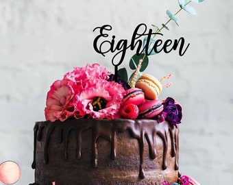 May include: A chocolate cake with chocolate ganache dripping down the sides, decorated with pink and purple flowers, macarons, and raspberries. The cake is topped with a black acrylic cake topper that says "Eighteen".