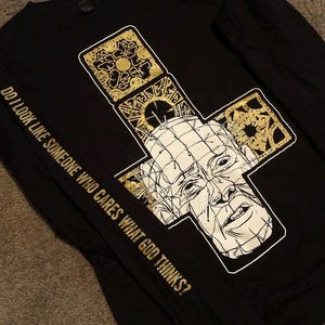 May include: Black long-sleeve shirt with a gold and white graphic of a character from the movie Hellraiser. The text "Do I look like someone who cares what god thinks?" is printed on the sleeve.