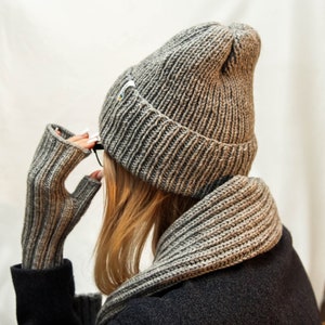 The focus of the image is a person viewed from the back, who is wearing a thick, knitted hat, prominently showcasing the texture and weave of the knit. The hat covers the head fully, leaving only a glimpse of blonde hair visible.