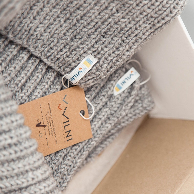 The picture shows a close-up of knit beanies with logo tags, and one has a cardboard tag indicating the brand and that it's handmade.