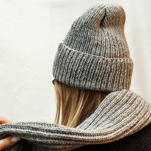 This image captures a close-up of a person wearing a textured, ribbed knit hat in shades of gray. The hat has a relaxed fit, with a noticeable, floppy point at the top, emphasizing its casual style.