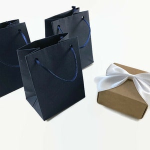 May include: Three dark blue paper gift bags with navy blue handles and a brown gift box with a white satin ribbon.