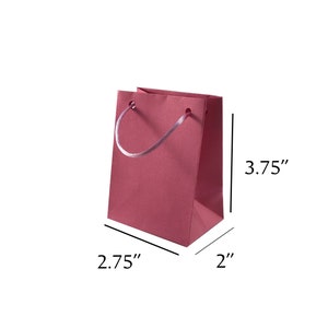 May include: A small, pink gift bag with white rope handles. The bag measures 3.75 inches tall, 2.75 inches wide, and 2 inches deep.