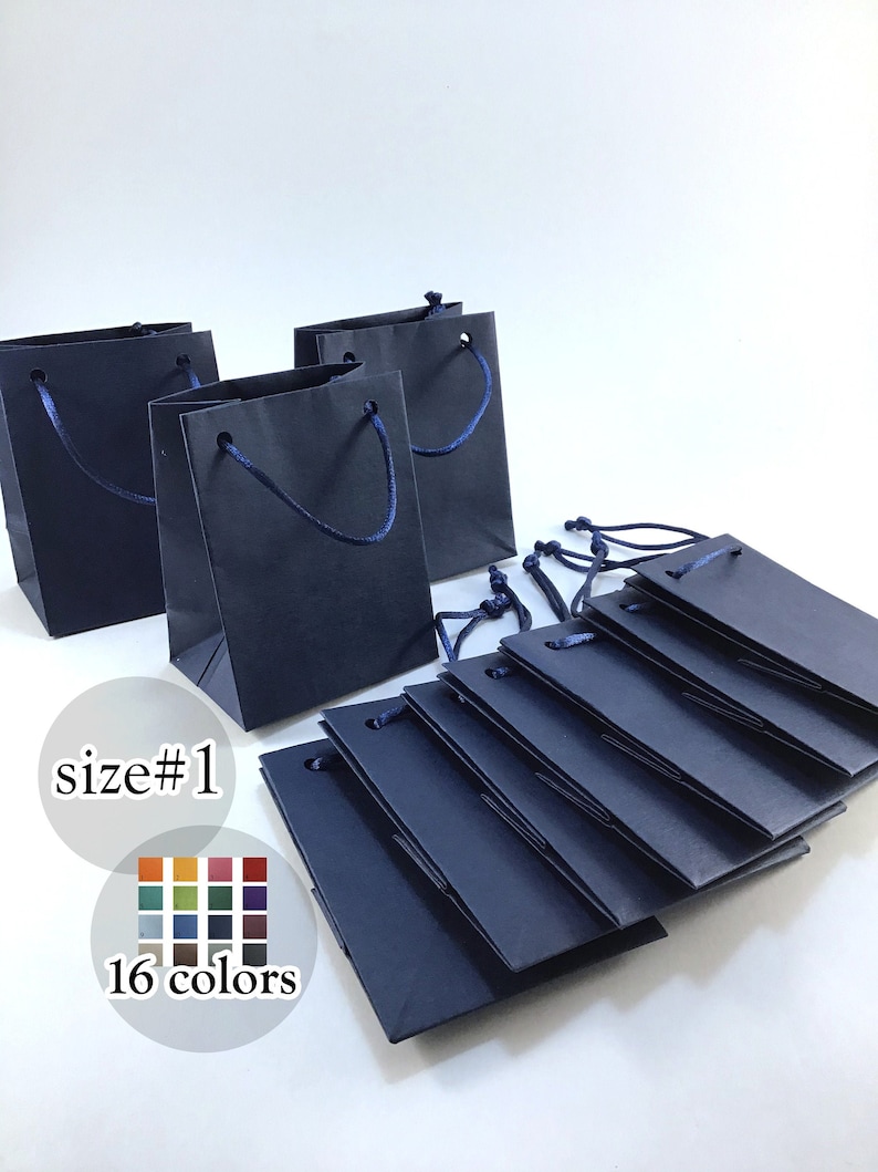 May include: A stack of 10 small navy blue gift bags with blue rope handles. The bags are folded flat and stacked on top of each other. The text "size #1" and "16 colors" is printed below the bags.