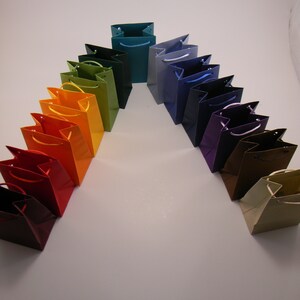 May include: A rainbow of colorful paper gift bags arranged in an arch shape. The bags are made of a sturdy paper and have a variety of colors, including red, orange, yellow, green, blue, purple, and brown.