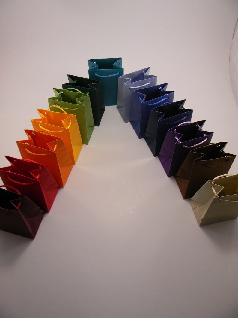 May include: A rainbow of colorful paper gift bags arranged in an arch shape. The bags are made of a sturdy paper and have a variety of colors, including red, orange, yellow, green, blue, purple, and brown.