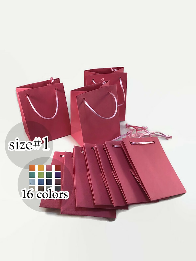 May include: A set of 10 small pink paper gift bags with pink ribbon handles. The bags are arranged in a pile, with some of the bags standing upright and others lying flat. The text "size#1" and "16 colors" are visible in the image.