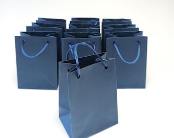 May include: A group of small, dark blue paper gift bags with blue ribbon handles. The bags are arranged in rows, with the front row slightly offset from the back row.