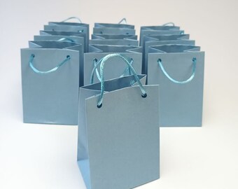 May include: A group of light blue gift bags with blue ribbon handles. The bags are arranged in a heart shape.
