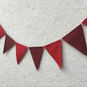K&ouml;nnte beinhalten: Eine Girlande aus roten und weinroten Wimpeln. Die dreieckigen Flaggen sind mit einer wei&szlig;en Schnur verbunden. Ein dekoratives Element f&uuml;r Partys, Feiern oder die Raumdekoration.