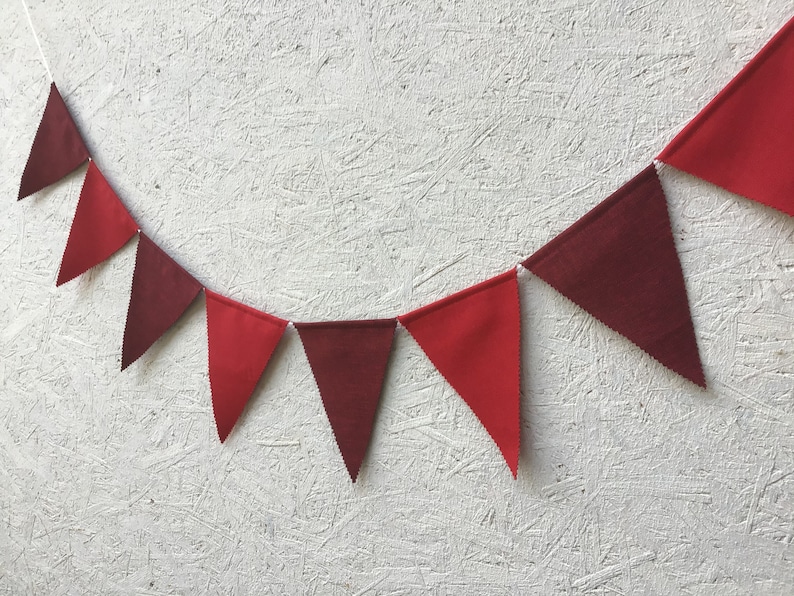 K&ouml;nnte beinhalten: Eine Girlande aus roten und weinroten Wimpeln. Die dreieckigen Flaggen sind mit einer wei&szlig;en Schnur verbunden. Ein dekoratives Element f&uuml;r Partys, Feiern oder die Raumdekoration.