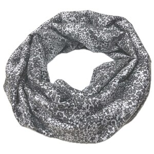 Könnte beinhalten: Ein weiß-schwarzer gemusterter Infinity-Schal. Der Schal ist aus weichem, dehnbarem Stoff gefertigt und perfekt, um jedem Outfit einen Hauch von Stil zu verleihen.