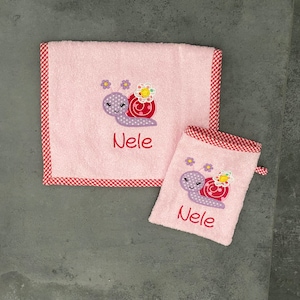 Könnte beinhalten: Rosa Handtuchset mit rot-weißem Karobord. Die Handtücher sind mit einem gestickten Schnecken mit einer Blume und dem Namen "Nele" verziert.
