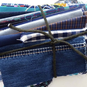 Könnte beinhalten: Ein Bündel verschiedener Stoffreste in Blautönen, Denim und gemusterten Textilien. Die Stoffe sind mit einem dunkelgrünen Seil zusammengebunden. Enthält Denim, Karos und unifarbene Stoffe.