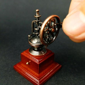 May include: A miniature antique-style coffee grinder with a wooden base and a metal grinder mechanism. The grinder has a crank that can be turned to grind coffee beans.